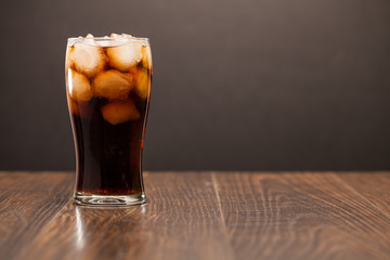 cola in glass with lemon and ice on wood table