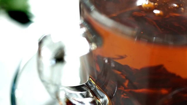 Spoon stirs the brew tea in a transparent cup