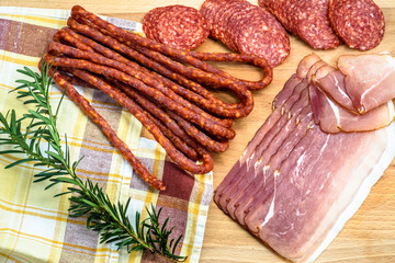 Assortment of meats: kabanos, salami, prosciutto slices on wooden background