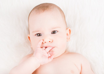 Closeup portrait of a lovely baby lying on white fur and sucking fingers