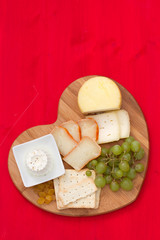 cheese with cookies, grapes on tray heart on red wooden background