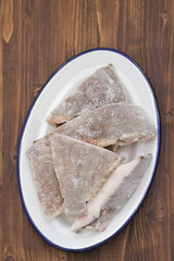frozen fish in white dish in brown wooden background
