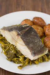 cod fish with potato and vegetables on white plate and glass of water on brown wooden background