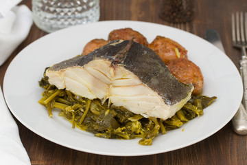 cod fish with potato and vegetables on white plate and glass of water on brown background