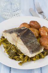 cod fish with potato and vegetables on white plate and glass of water on blue wooden background