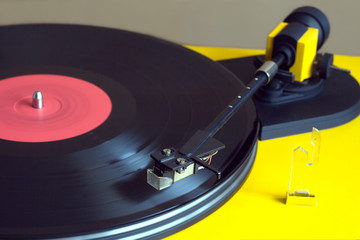 Playing vinyl LP record with red label on turntable with yellow case. Horizontal photo closeup