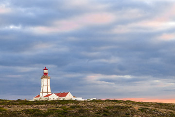 Fototapeta na wymiar The Espichel Cape lighthouse, an 18th century building during sunset and a storm sky. Sesimbra, Portugal.