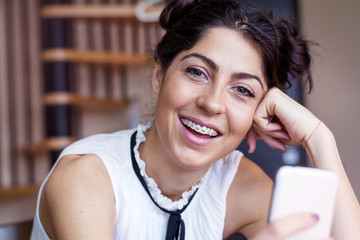 Portrait of young smiling woman with braces using smart phone