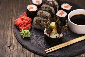 Assortment of sushi rolls with salmon and vegetables, served with soy sauce and chopsticks over grunge wooden background. Selective focus
