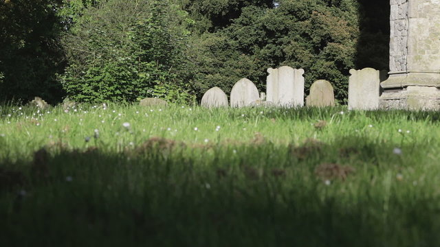 Old English churchyard. The sun creating movements of shadow on the grass of a traditional old English churchyard, grave stones and church wall.