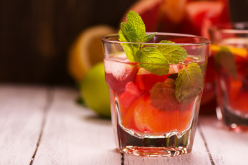 Sangria with citrus fruits, ice cubes and mint leaves in glasses over wooden background. Selective focus