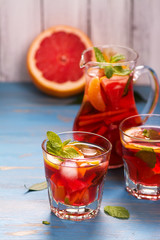 Jug and glasses with homemade citrus lemonade with mint and ice cubes over wooden background. Selective focus
