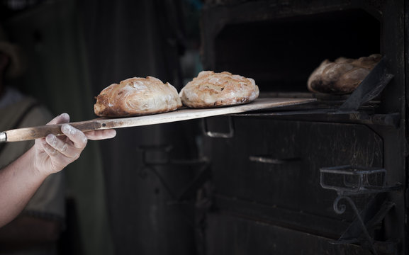 Close-up of a man baker introducing breads in a classic oven  