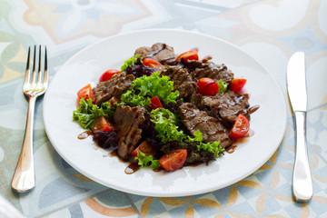 Warm salad with beef, tomatoes and lettuce on a white plate