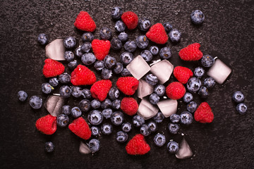 Ripe blueberry and raspberry with ice cubes over black wet stone background. Toned image. Selective focus