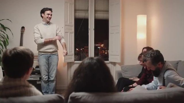 Young adult man playing charades at home with friends at night. People find out solution and start laughing. 4K, UHD