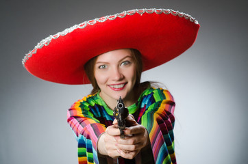 Girl in mexican vivid poncho holding handgun against gray