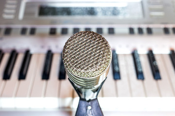 Silver microphone on a rack in the center close-up. Keyboard synthesizer in the background....