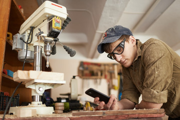 Worker in glasses near the machine drills to break looking at phone