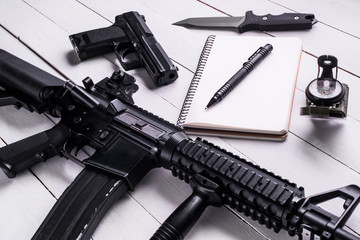 Notebook,pen,rifle,pistol,knife and compass on table.Top view/Open notebook with pen,assault rifle,gun,military knife  and compass on the wooden table