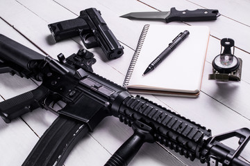 Notebook,pen,rifle,pistol,knife and compass on table.Top view/Open notebook with pen,assault...