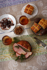 Traditional easter dinner set with sliced meat, bread with herbs, handmade colored eggs, chocolates, easter cake and glasses of juice on colorful tablecloth
