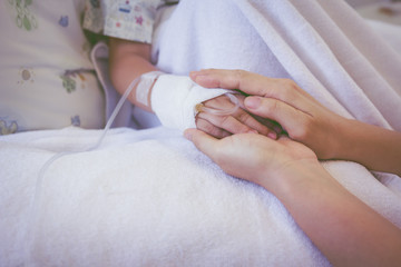 Close up hand of parent holding hand of child in hospital. Retro style.