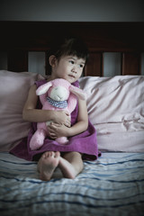Little sad asian girl sitting on bed.