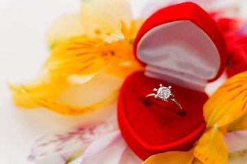 Engagement diamond ring in red gift box on pile of flower petals.  Symbol of love and marriage.