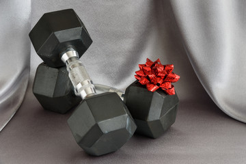 Set of black and silver dumbbells with a red bow on a silver background
