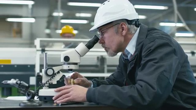 Senior engineer is inspecting a detail under microscope in a factory. Shot on RED Cinema Camera.