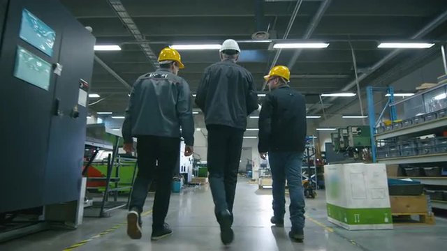 Back view of senior engineer and two workers are walking with papers through the factory space. Shot on RED Cinema Camera.