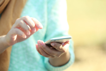 Female hands holding a mobile phone outdoors, on blurred background