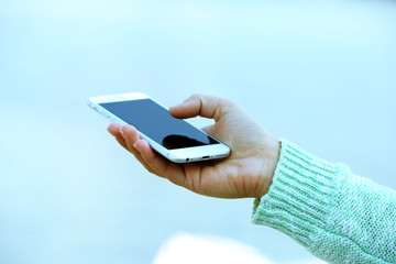 A female hand holding a mobile phone outdoors, on blurred background