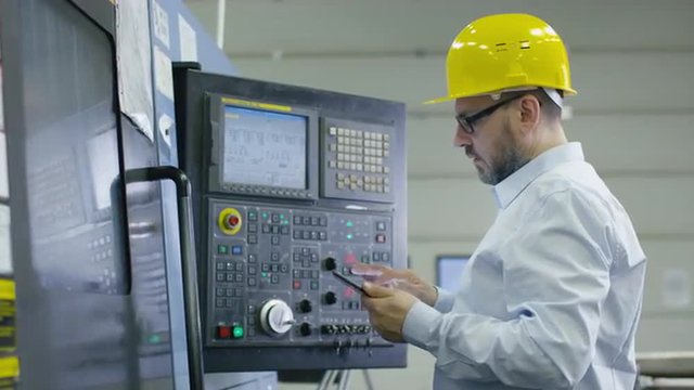 Engineer is programming a cnc milling machine with a tablet computer in a factory. Shot on RED Cinema Camera.