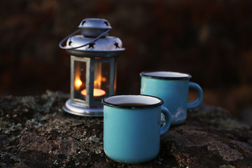 Decorative lamp and two blue mugs on rock in mountains