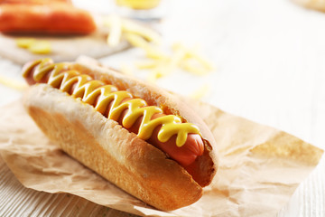 Hot dog with fried potatoes on craft paper on wooden background