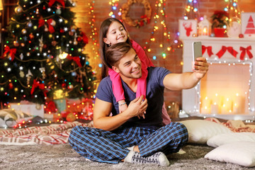 Older brother and little sister taking photo of their self with smart phone in Christmas living room