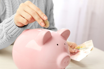 Woman putting euro coin and banknotes into a piggy bank on the table. Financial savings concept