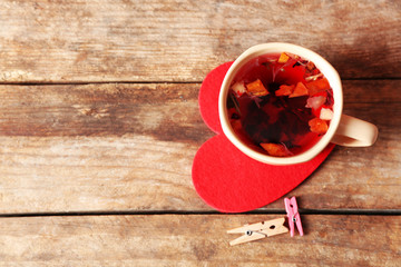 Cup of fruit tea on red heart with clothespins on wooden background closeup