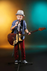 Naklejka premium Little boy playing guitar and singing with microphone on a dark lighted background