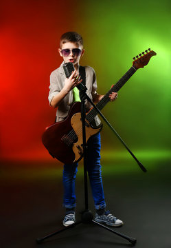 Little boy playing guitar and singing with microphone on a bright background