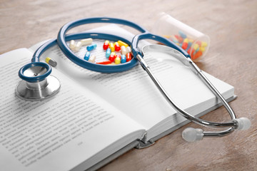 Stethoscope with pills and book, closeup