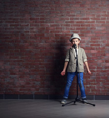Fototapeta na wymiar Little boy singing with microphone on a brick wall background