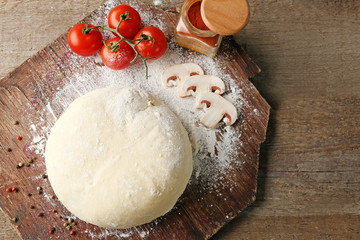 Fresh prepared dough with tomatoes and sliced mushrooms on a wooden board, close up