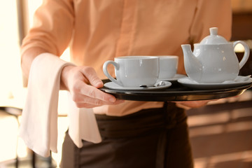 Waiter holding tray with teapot and cups close up