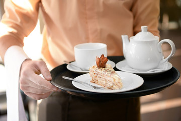 Waiter holding tray with teapot, cups and cake close up