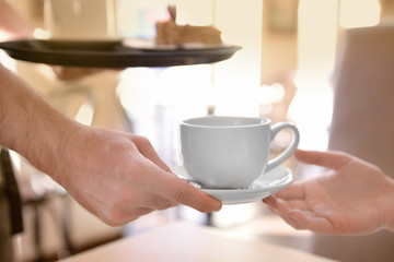 Waiter serving tea to customer in cafe