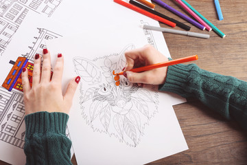 Female hand painting anti stress colouring with orange felt pen