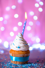 Cupcake with white cream icing and candle on a glitter background, close up